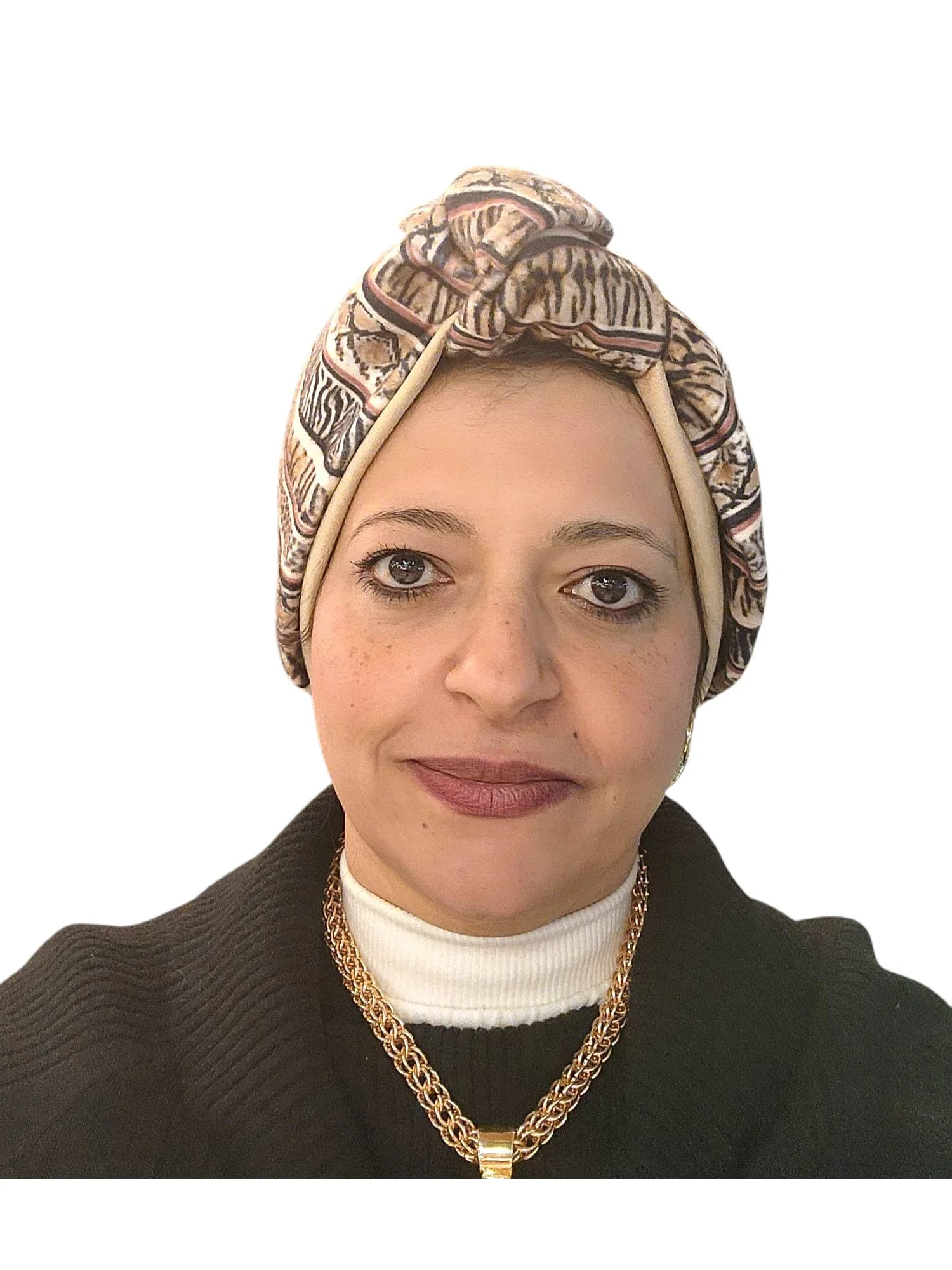 Close-up of a woman with light skin, wearing a patterned headscarf, a black sweater over a white turtleneck, gold jewelry, and makeup with dark eyeliner and lipstick.