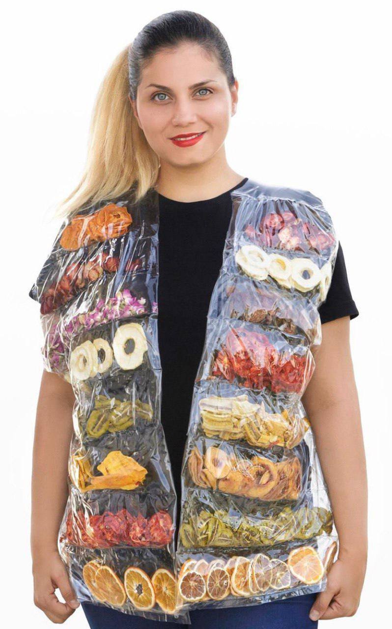 Woman with blonde hair, blue eyes, and red lipstick wearing a black shirt and a transparent plastic vest filled with dry fruit slices.