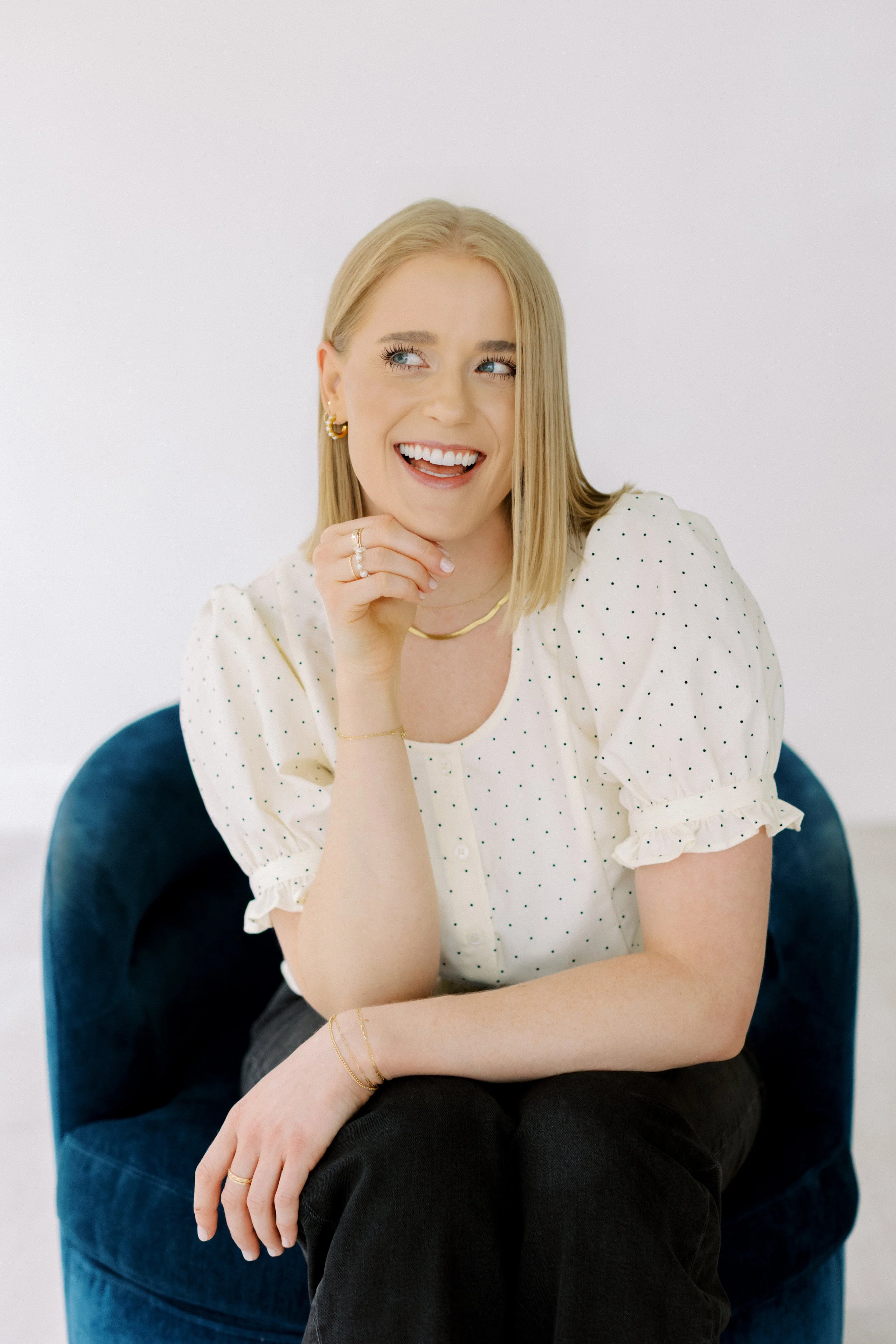 A woman with blonde hair smiling, sitting in a blue velvet chair, wearing a white polka dot blouse and gold jewelry. Emily Rucker M.A. LPC. Houston Texas. Alive and Whole Wellness. Christian Counseling. EMDR. Trauma. Anxiety.