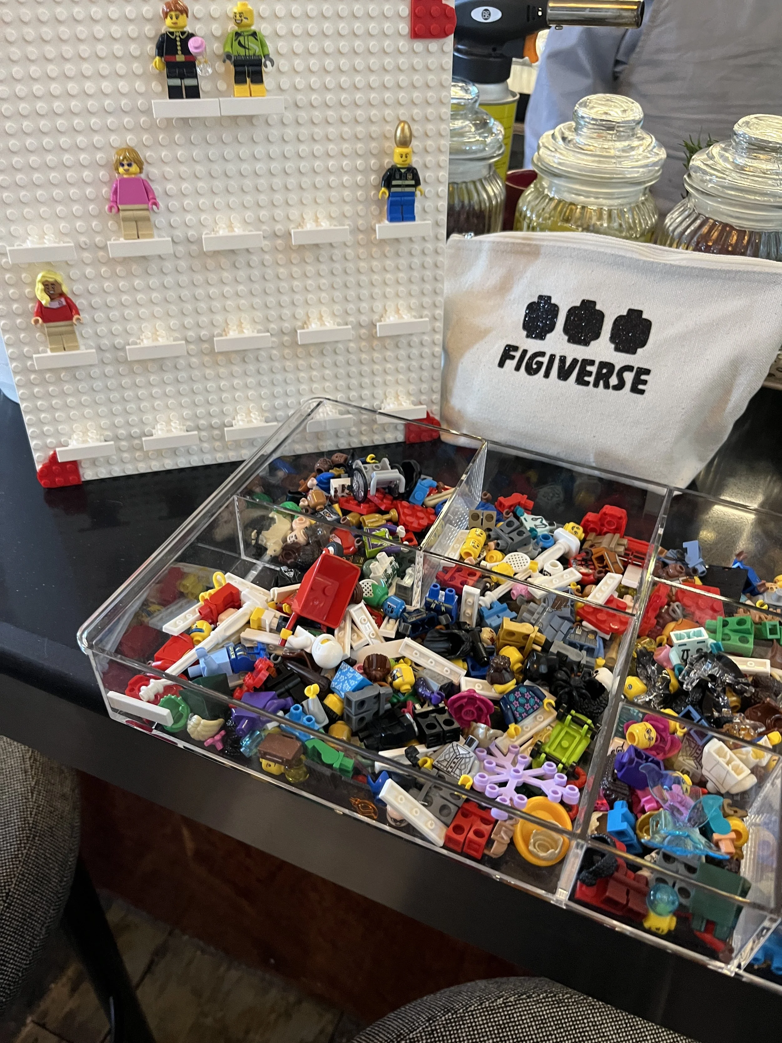 A display of LEGO minifigure pieces and assembled minifigures on a table at a LEGO set building or trading event.