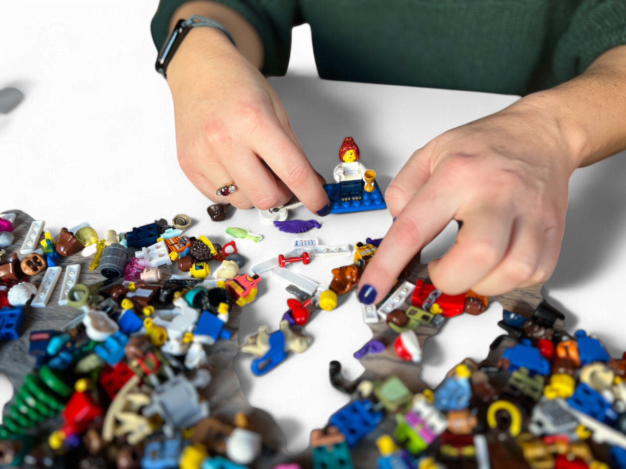 Person's hands assembling LEGO pieces on a black surface with scattered LEGO parts.