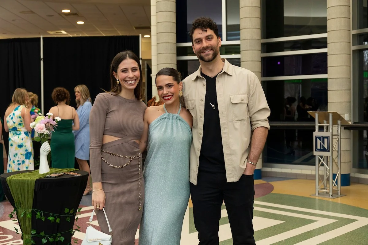 Three students pose together in the atrium to the Fashion Show