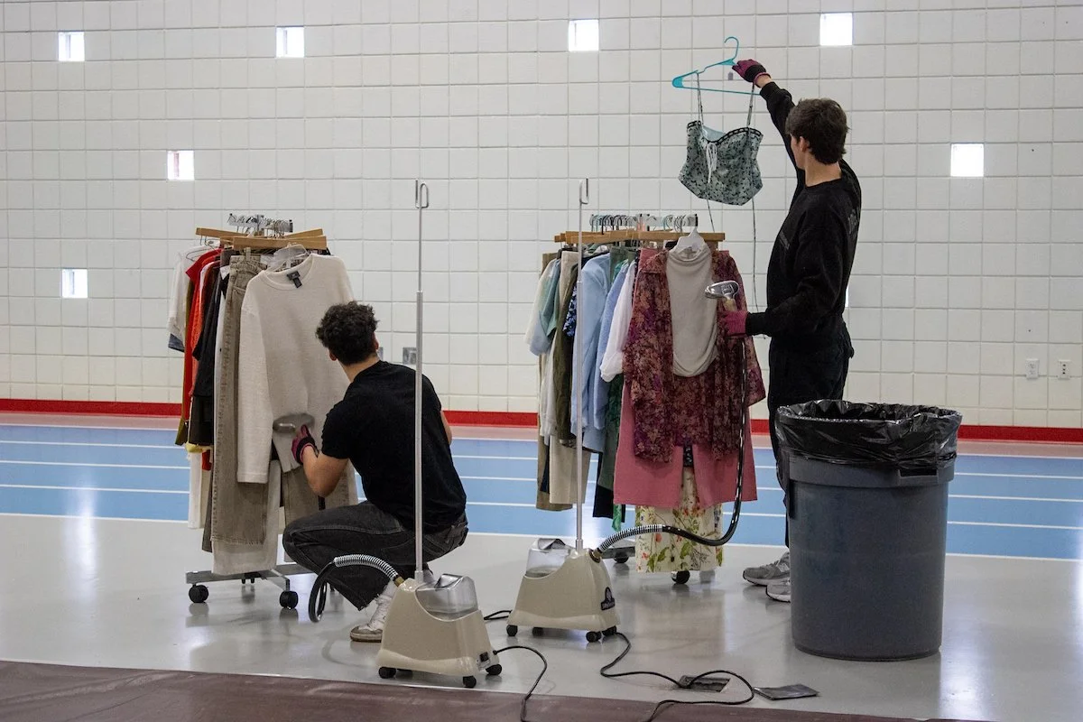Two students iron and prepare a clothing rack for the Fashion Show