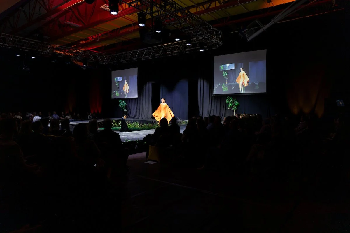 A woman in an orange dress poses on stage in a dark room