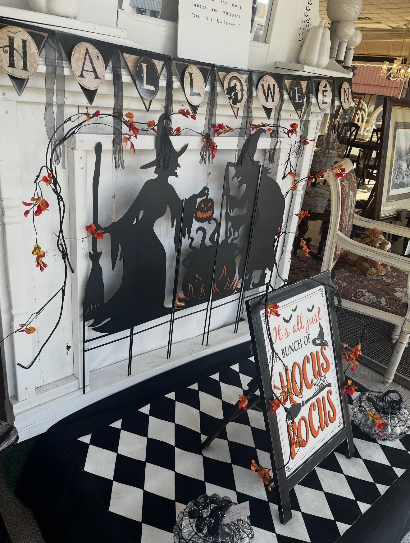 Halloween-themed display featuring black silhouette of a witch with a pointed hat and a pumpkin, along with a sign that reads 'It's all just a bunch of HOCUS POCUS'.