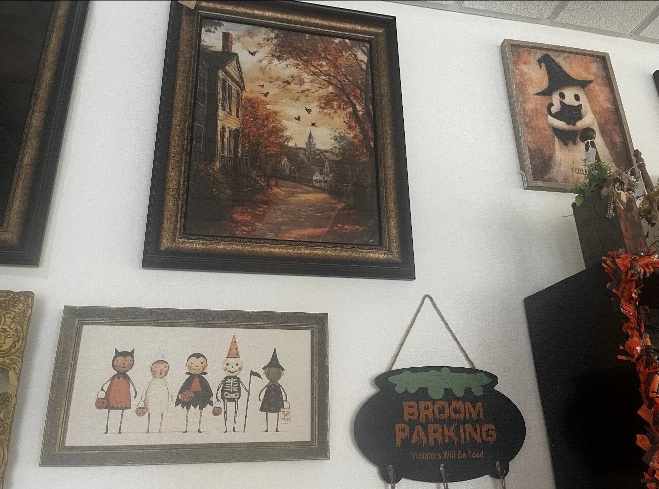 A wall decorated with Halloween-themed paintings and a sign that reads 'Room Parking Violators Will Be Toad.' The paintings include a spooky autumn scene and stylized Halloween characters.