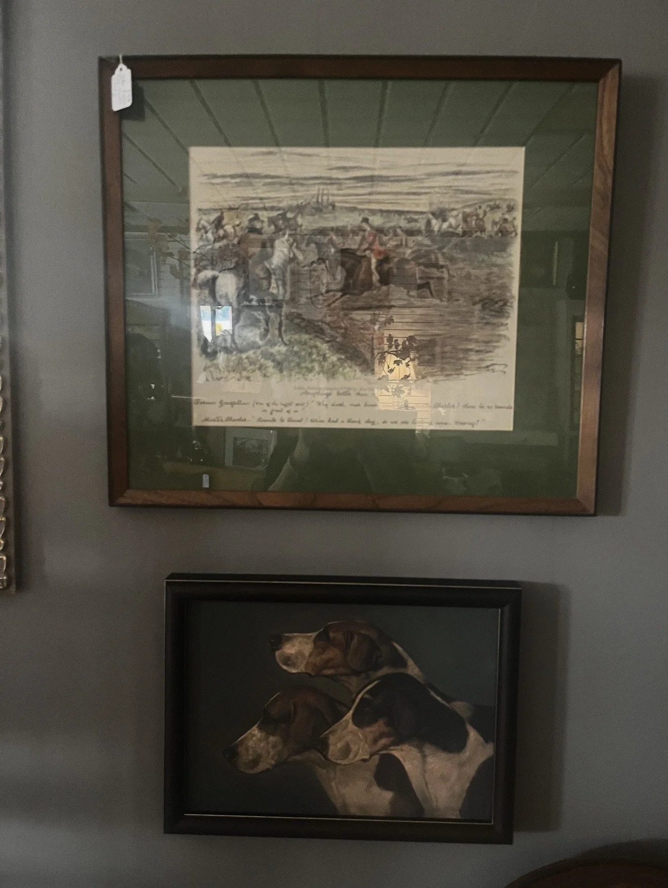 Framed artwork depicting a historical scene with horses and riders, hung on a gray wall, with a reflection of the ceiling visible on the glass.