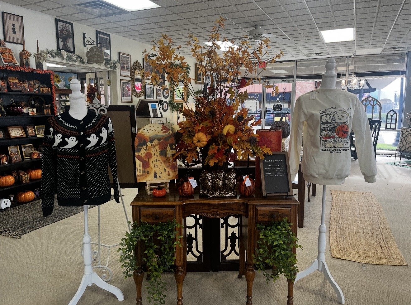 Indoor display of fall-themed decorations with a large floral arrangement, pumpkins, and sweaters on mannequins.
