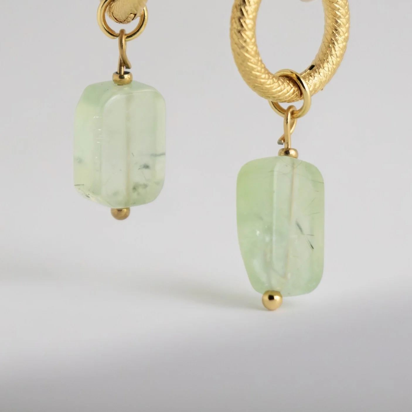A pair of gold hoop earrings with rectangular, light green semi-translucent stone charms hanging from small gold beads.
