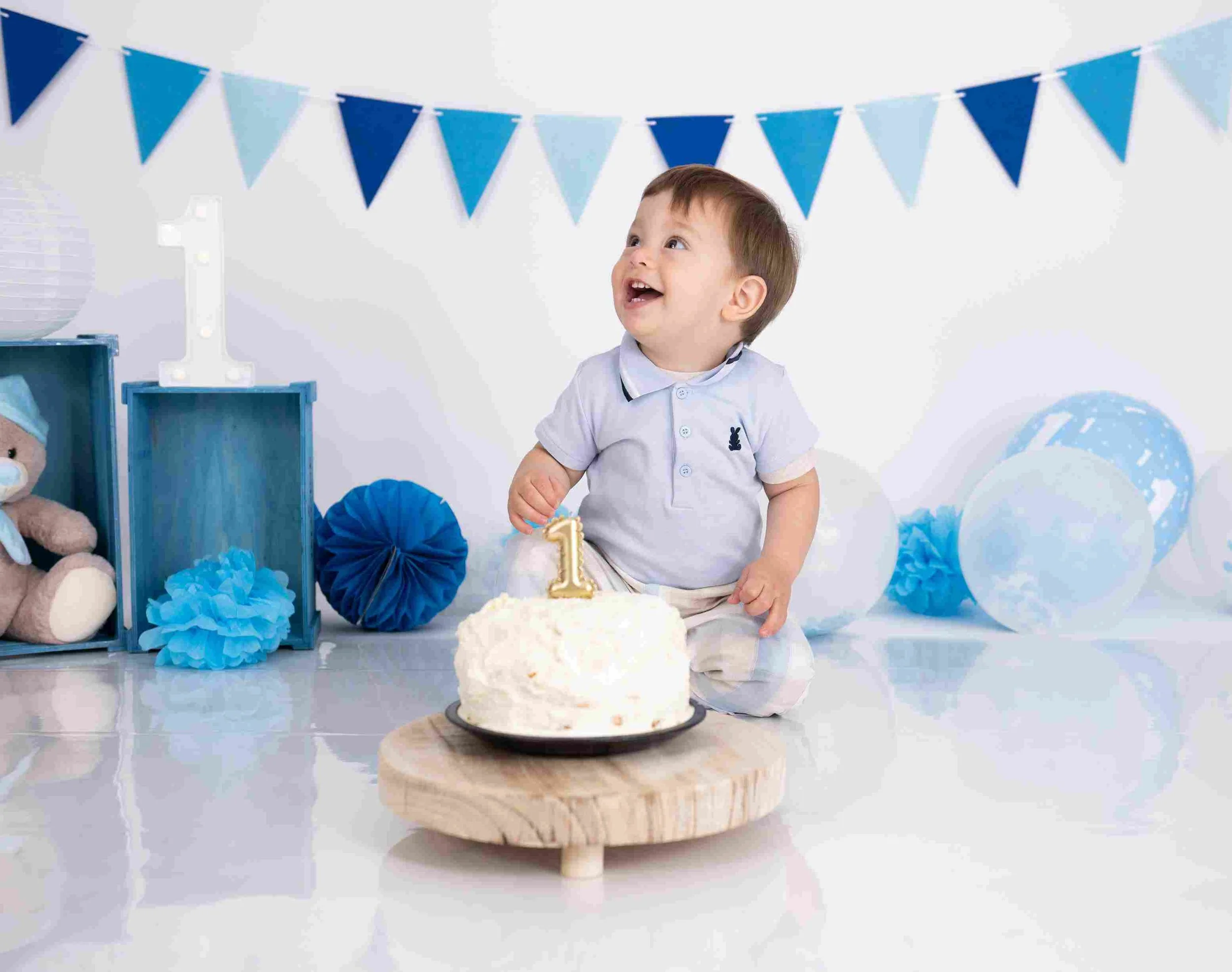 Baby boy in birthday hat holding number 1 prop during cake smash session in Dublin photography studio.