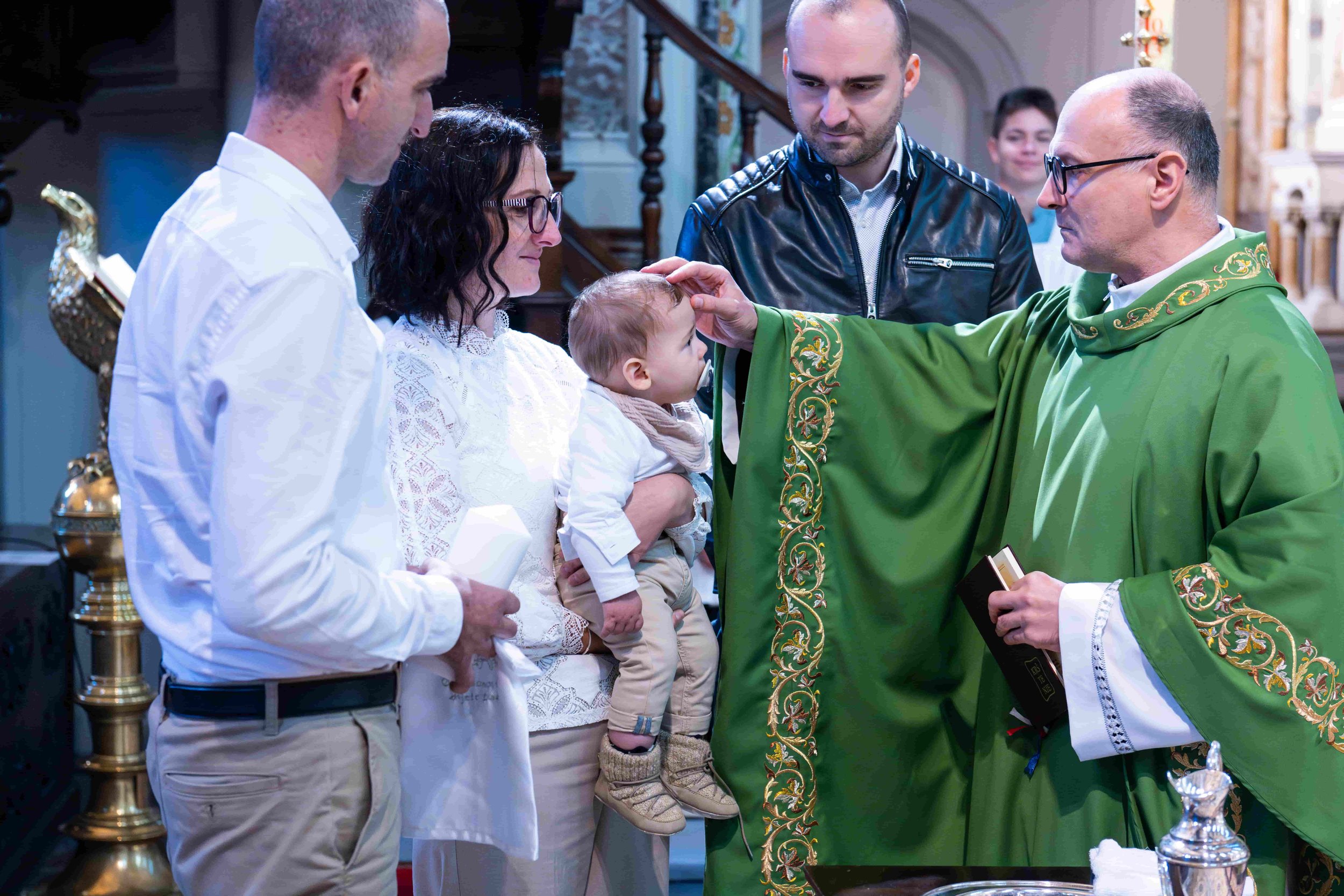 A beautiful christening ceremony is held in a church, capturing the precious moments of a baby’s baptism. The main images show a priest in traditional green vestments blessing the child and performing the baptism with holy water, surrounded by parent