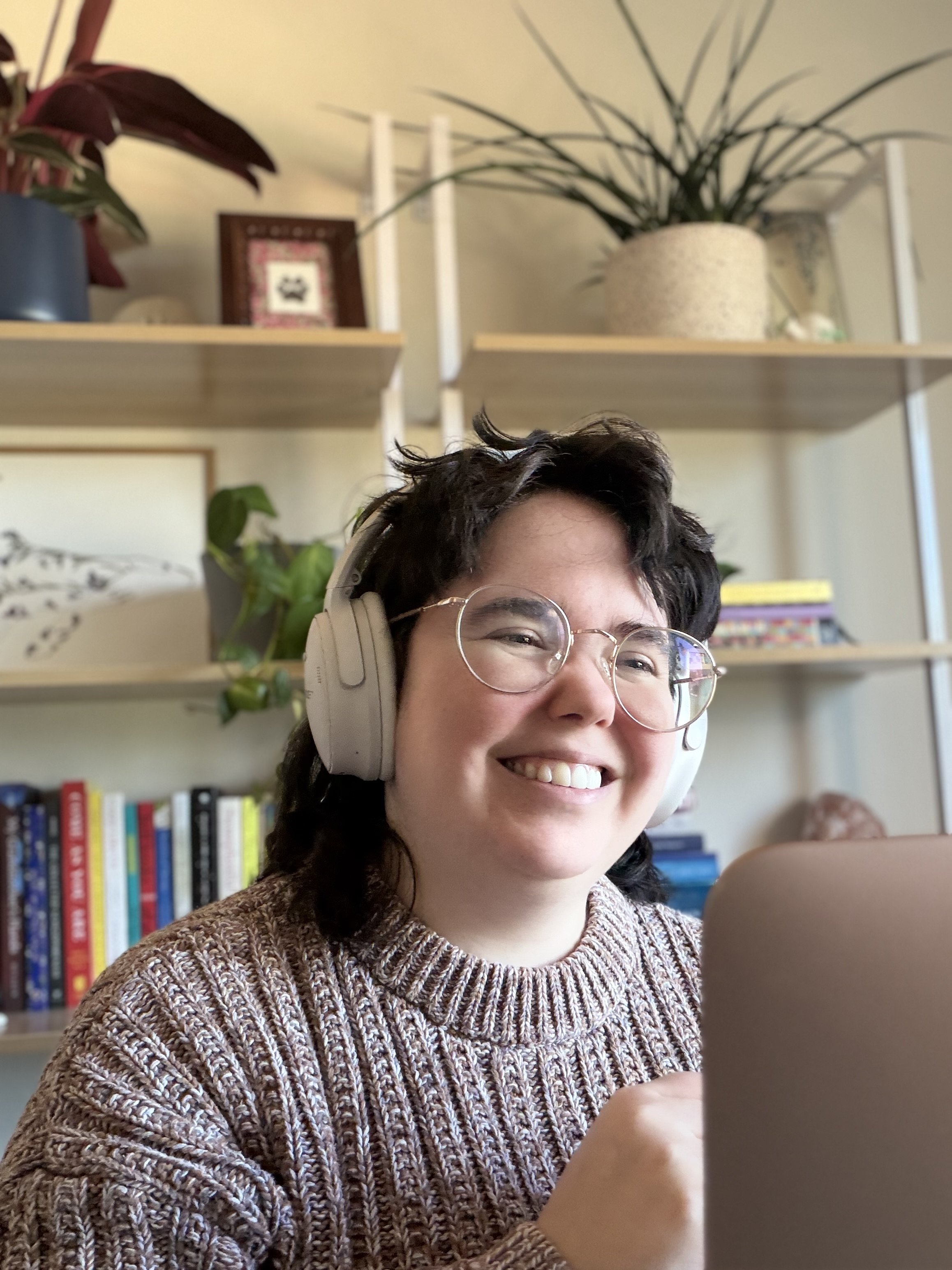 Pictured is Owen Wardrop, LCSW a white nonbinary person with a brown mullet, brown sweater, round glasses smiling providing telehealth therapy servicees.
