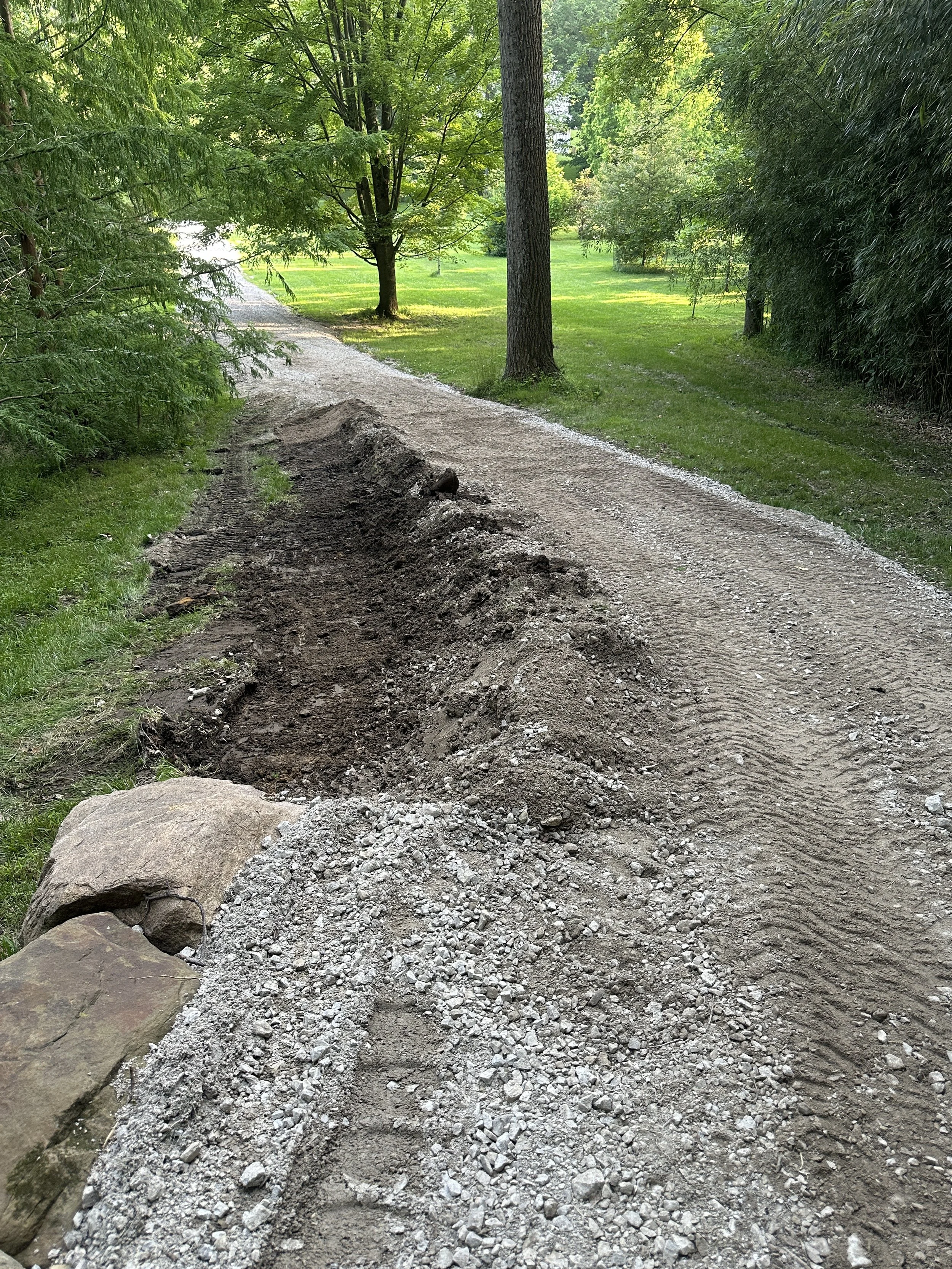 A gravel pathway under construction in a lush green park with trees and grass on either side.