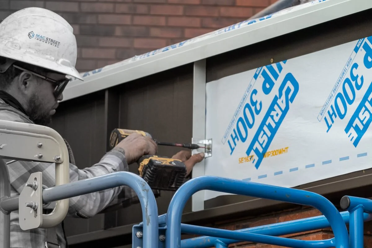 Roofer installing dark bronze standing seam architectural metal on a bank building's entry