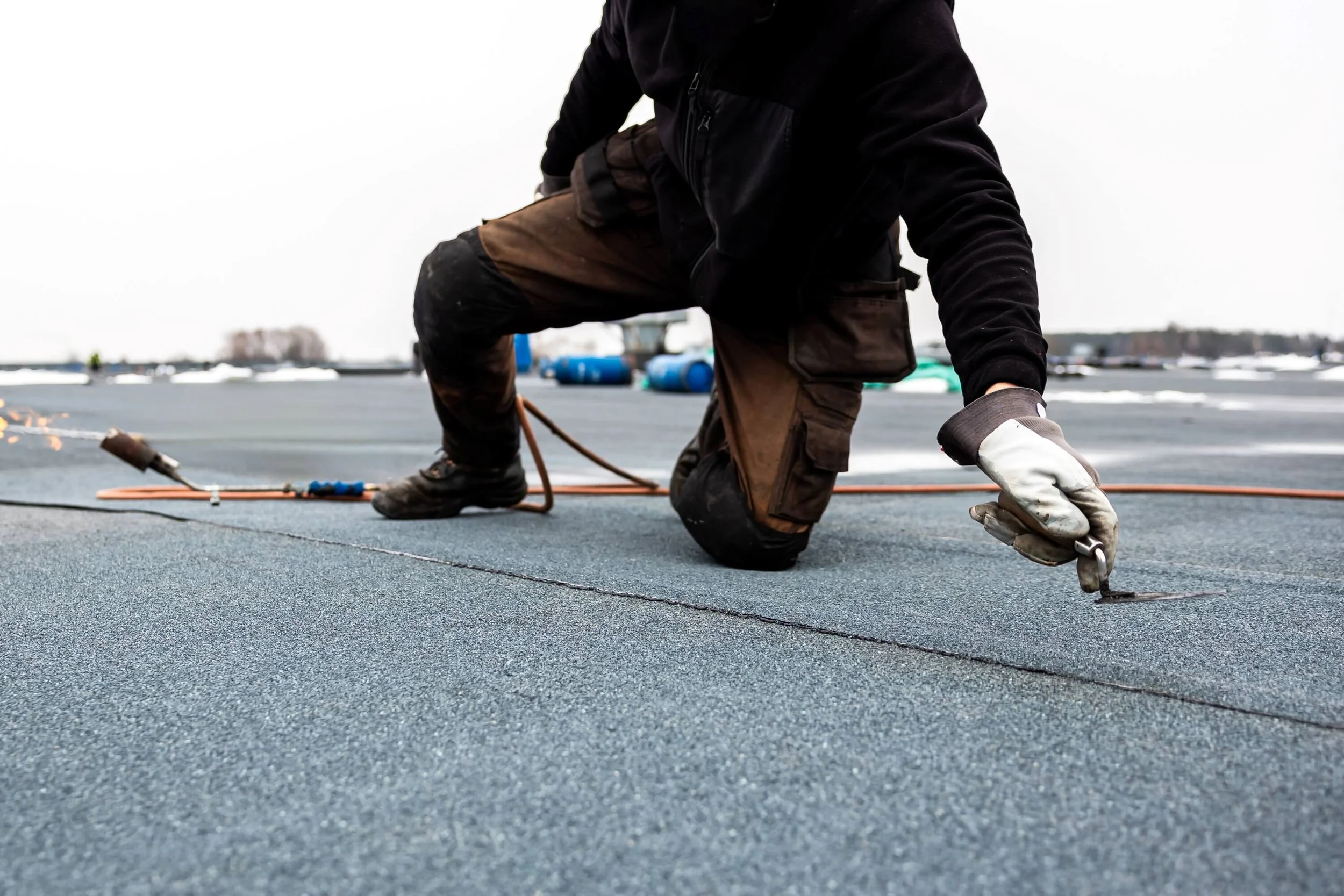 professional roofer applying bitumen roll on flat roof with a gas burner