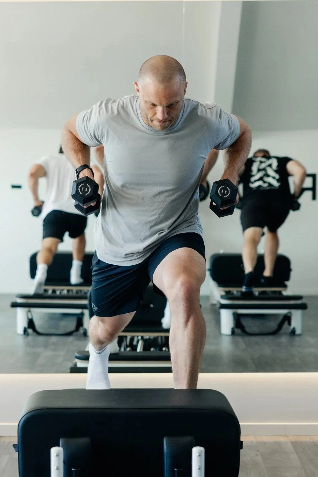 Image showcases male reformer pilates member executing a lunge with dumbbell row for strength and stability.