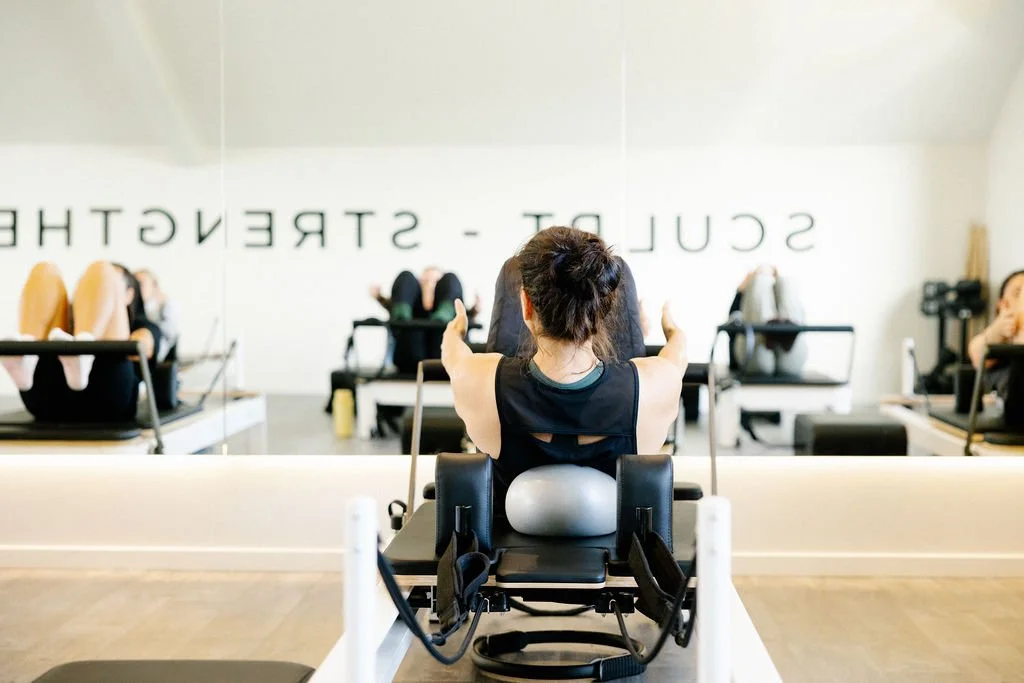 Lincoln Loft member executes an abdominal crunch with ball for stability on reformer pilates machine.