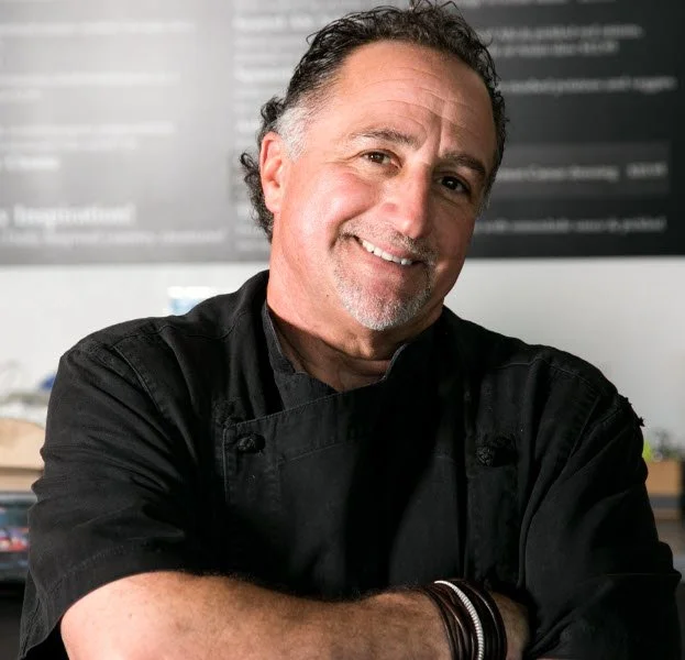 Chef Martin Corso smiling in a black chef's coat with arms crossed, standing in a kitchen.