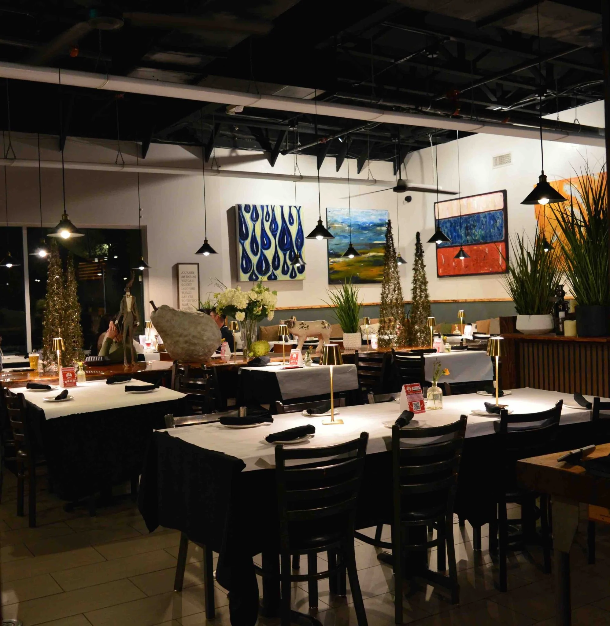 Interior of a decorated restaurant dining area with tables set for guests, artwork on the walls, and modern lighting.