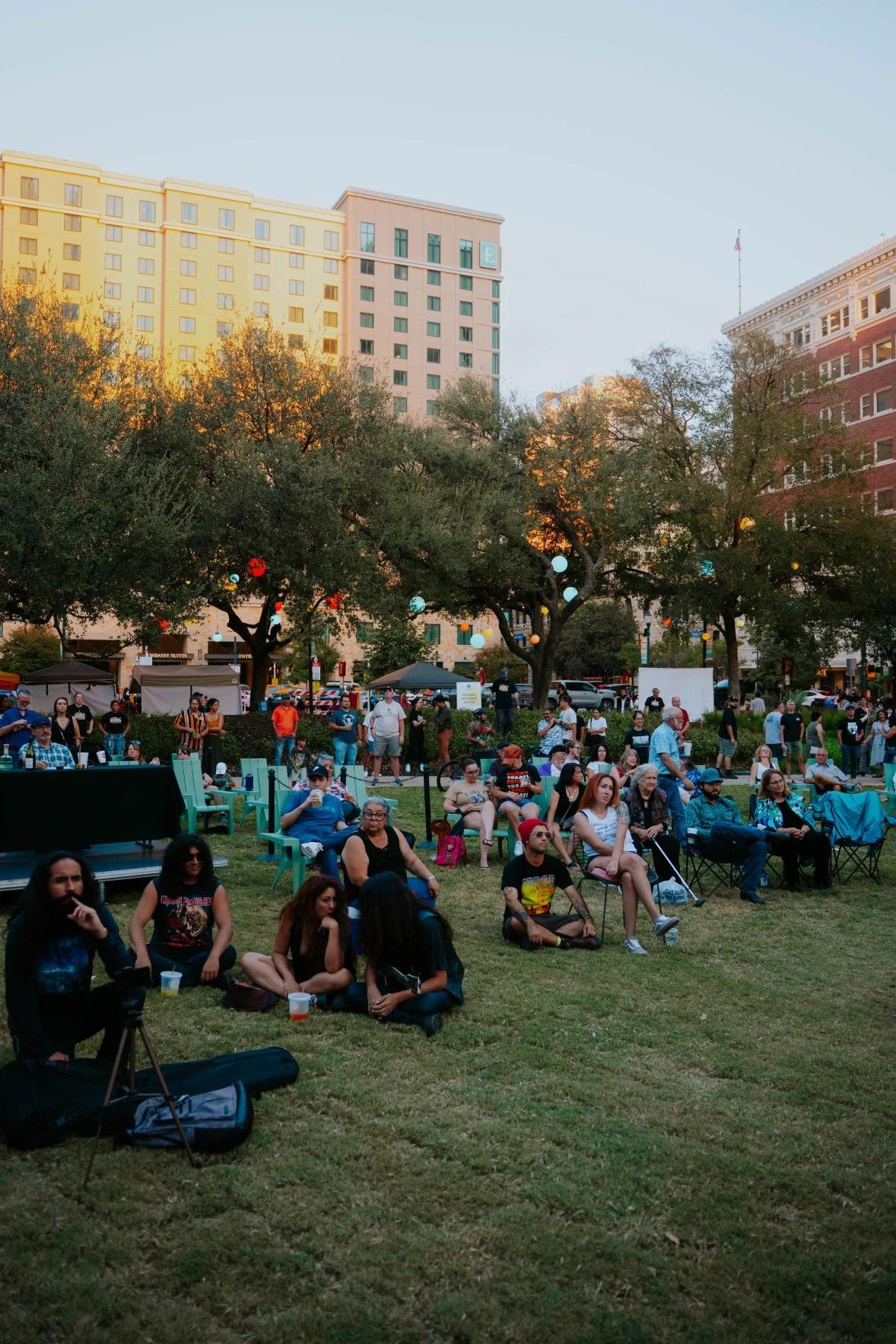 Wide view of a crowd gathered on a lawn in front of city buildings at an outdoor event.