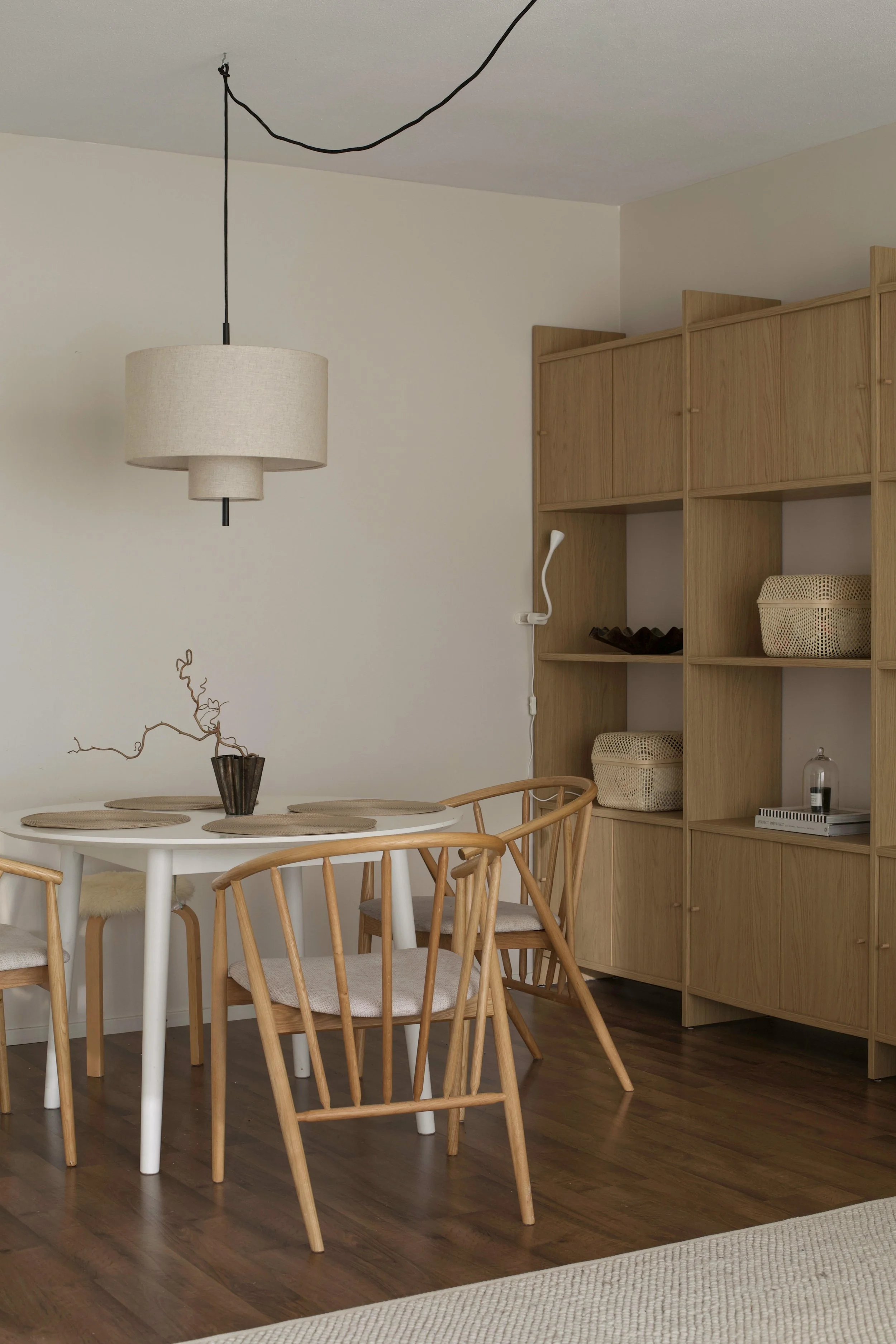 Lämpöä ja kodikkuutta saatiin lisäämällä kokonaisuuteen tammikuvioinen kirjahylly, beigen ja ruskean sävyjä valaisimen ja tekstiilien kautta sekä sijoittelemalla huonekalut sopivammin.