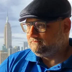 Photo shows Arun in glasses and a hat with the Empire State Building in the distance behind him
