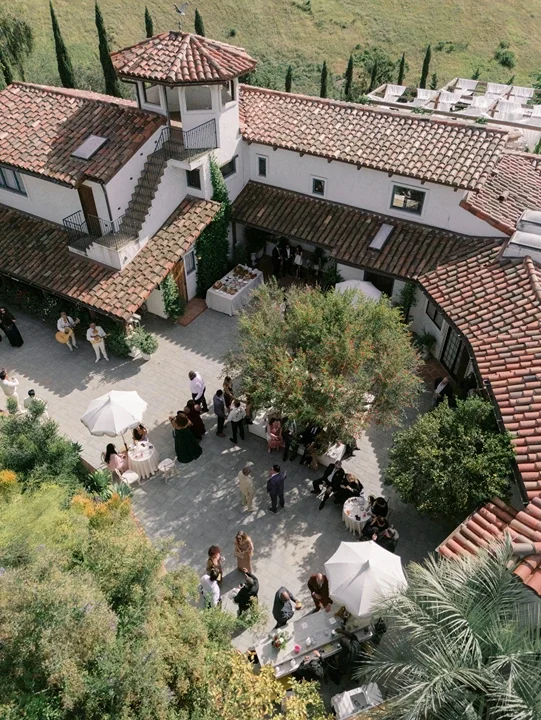 Aerial view of guests gathered for cocktail hour in the courtyard at Jeune Perché Estate, framed by terracotta rooftops and greenery