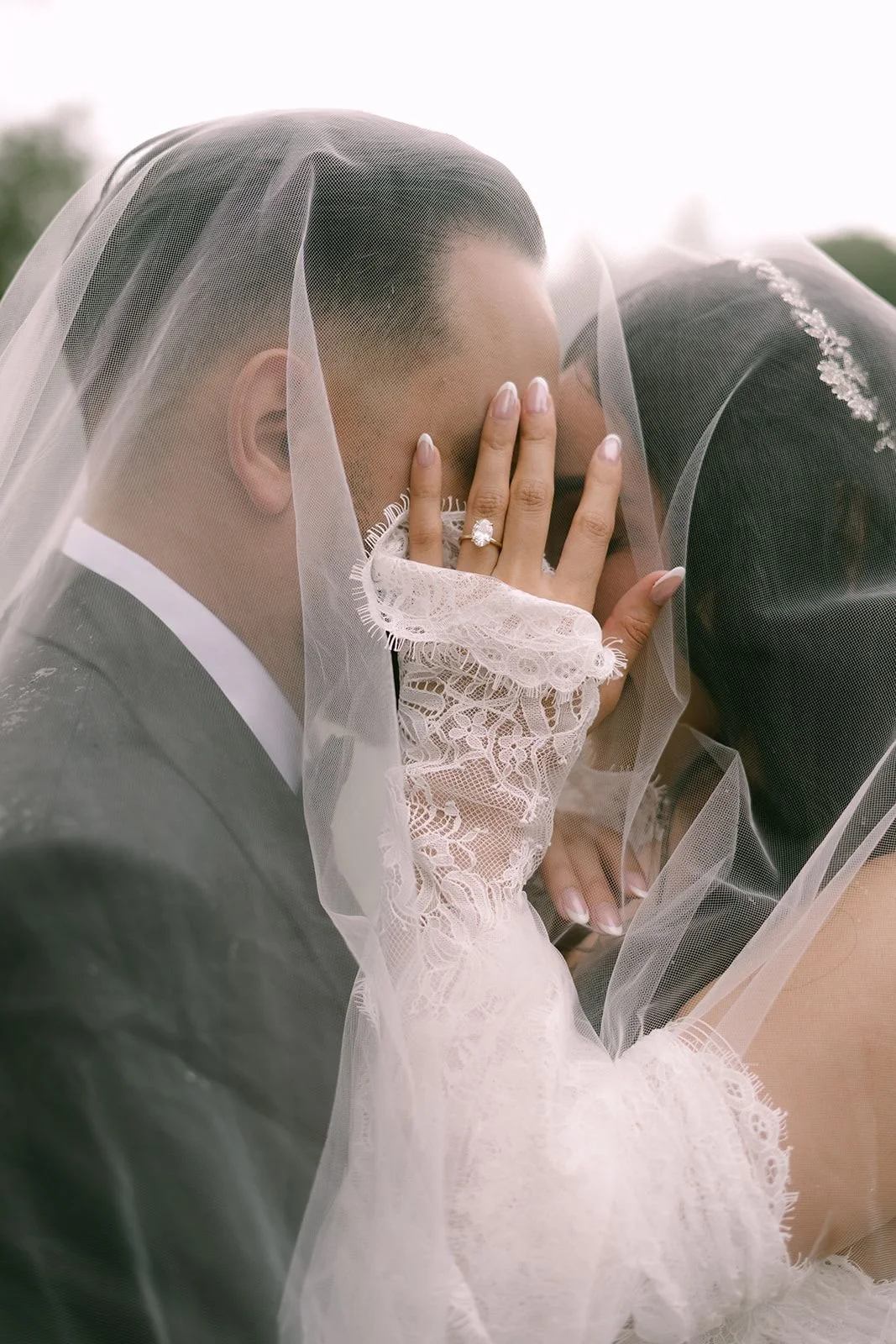 Bride and groom portrait with her hand covering their faces showcasing her engagement ring