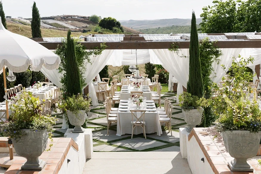 Elegant outdoor reception at Jeune Perché Estate with white draping, cypress trees, chandeliers, and long tables set with white and deep-red florals
