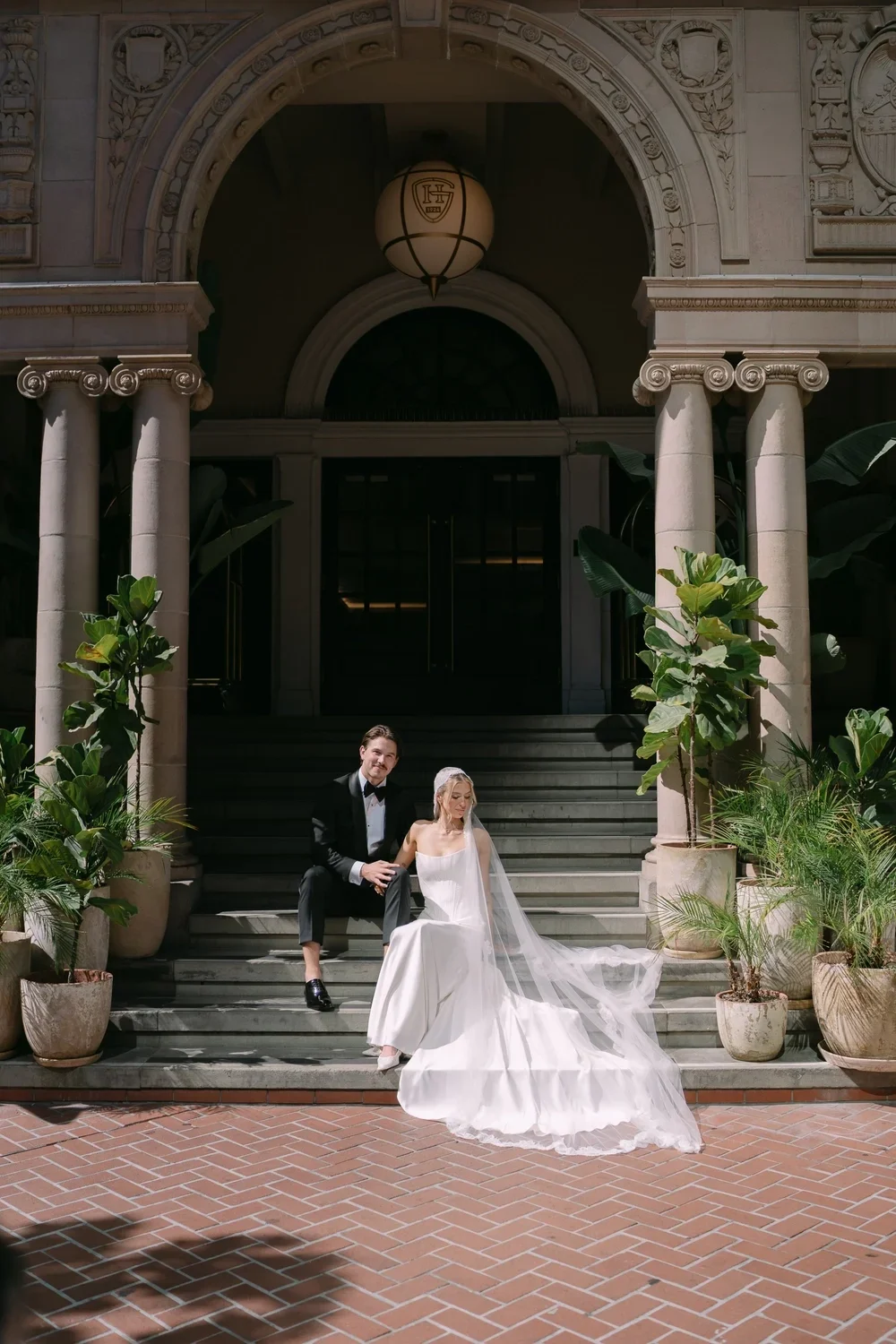 San Diego wedding photographer capturing a bride and groom sitting on the steps of The Guild Hotel, showcasing editorial wedding photography with the bride in a flowing gown and veil.