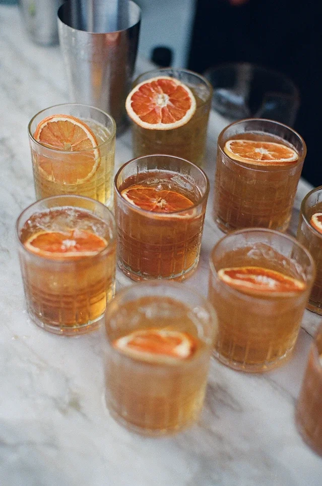 Signature cocktails garnished with dried orange slices on a marble bar during cocktail hour at Jeune Perché Estate