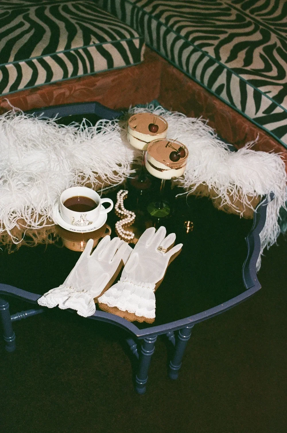 A close up of wedding details including gloves, diamond ring, pearl necklace and dessert in a moody Lafaeytte Hotel room, captured on 35 mm film