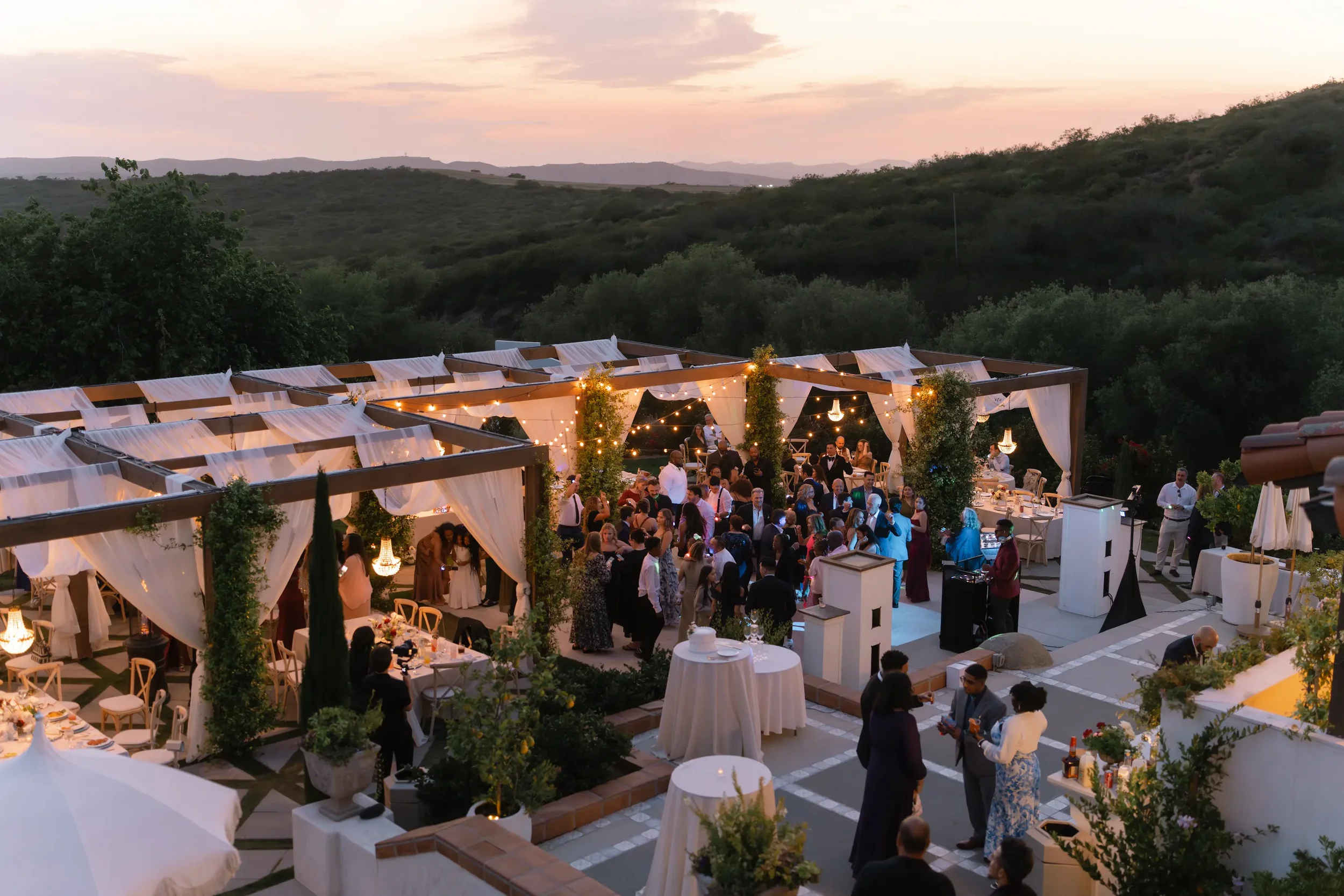 Guests mingling at the golden-hour reception under a string-lit tented pergola overlooking rolling hills at Jeune Perché Estate