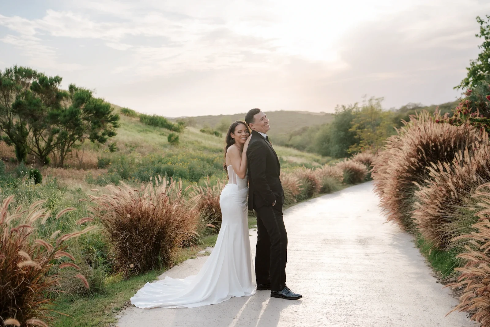 Bride and groom embracing at sunset on a grass-lined path during their Jeune Perché Estate wedding