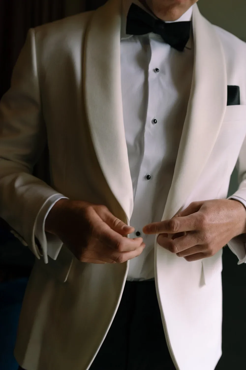 Close-up of groom fastening his tuxedo cufflinks before the wedding ceremony, showcasing attention to detail in the preparations.