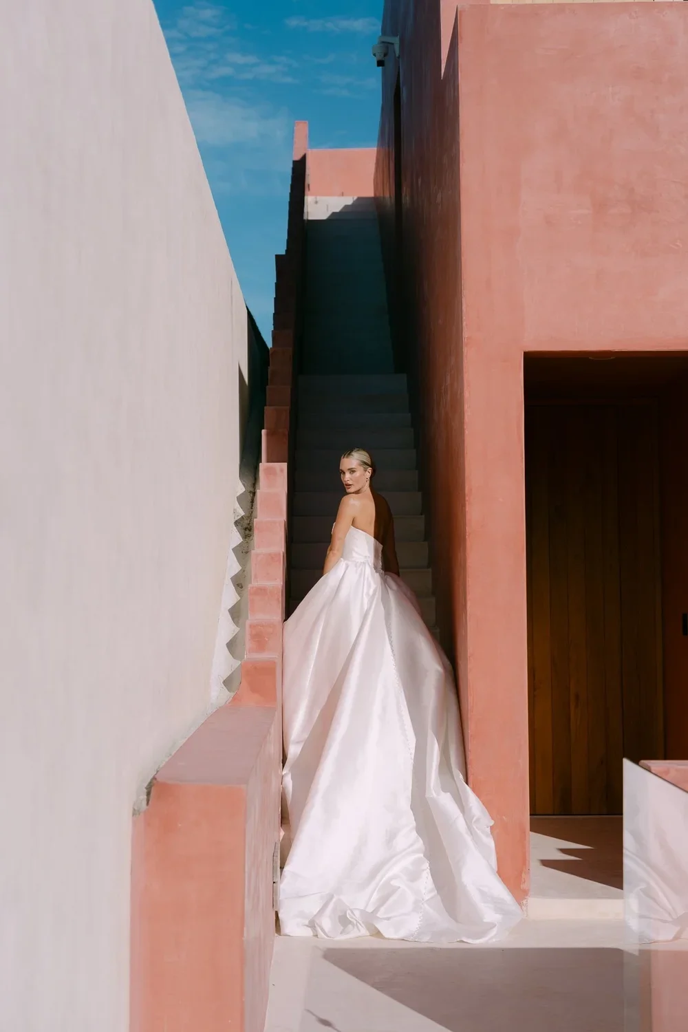 Bride walking up a staircase in Tulum in her wedding gown, captured in a serene moment with sunlight illuminating the scene.