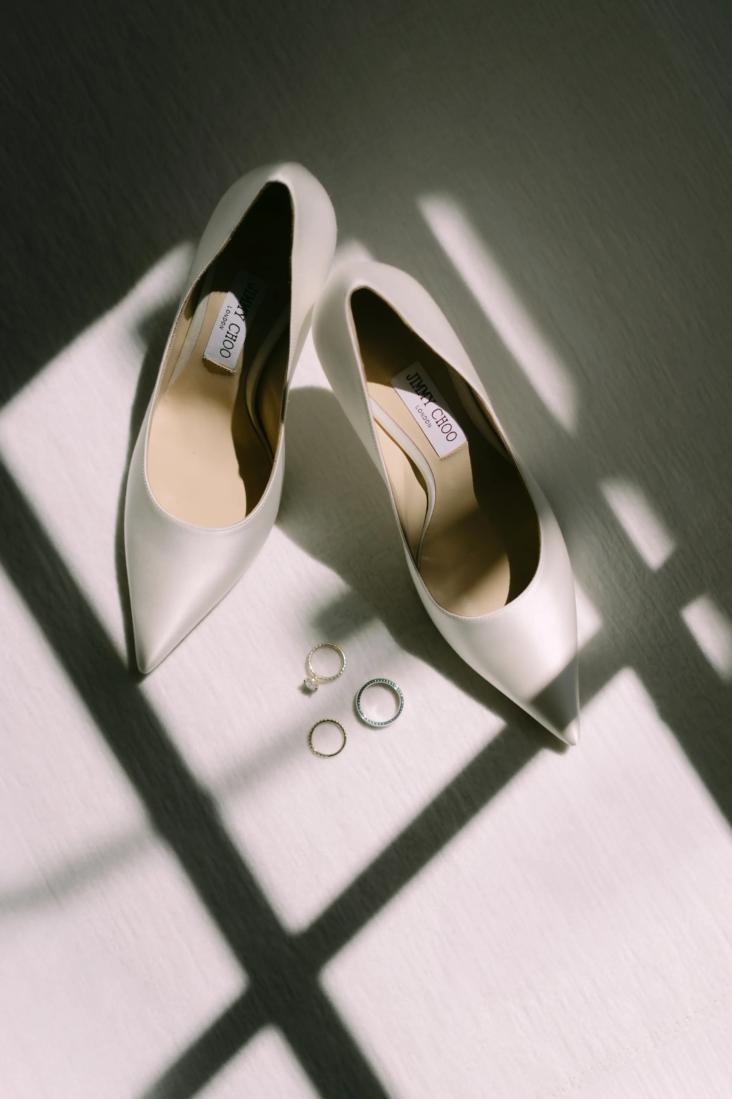 Close-up of bride’s Jimmy Choo wedding shoes with wedding rings placed beside them, with soft lighting highlighting the elegance of the moment.
