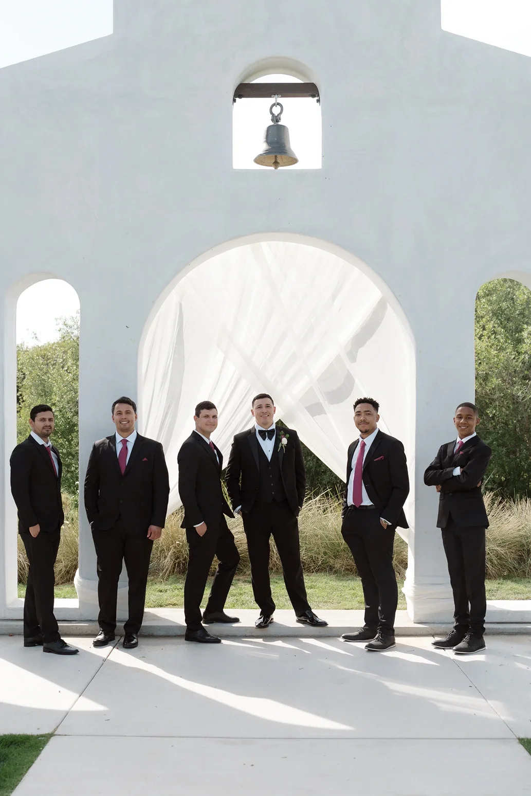 Groom and his groomsmen in black suits posing beneath the draped ceremony arch at Jeune Perché Estate