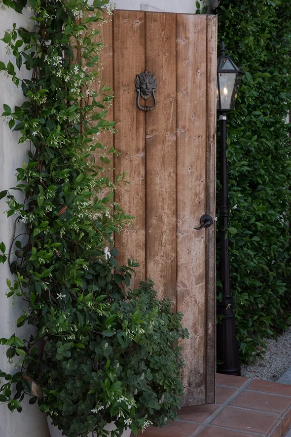 Rustic wooden entry door with a lion's-head knocker framed by climbing jasmine at Jeune Perché Estate