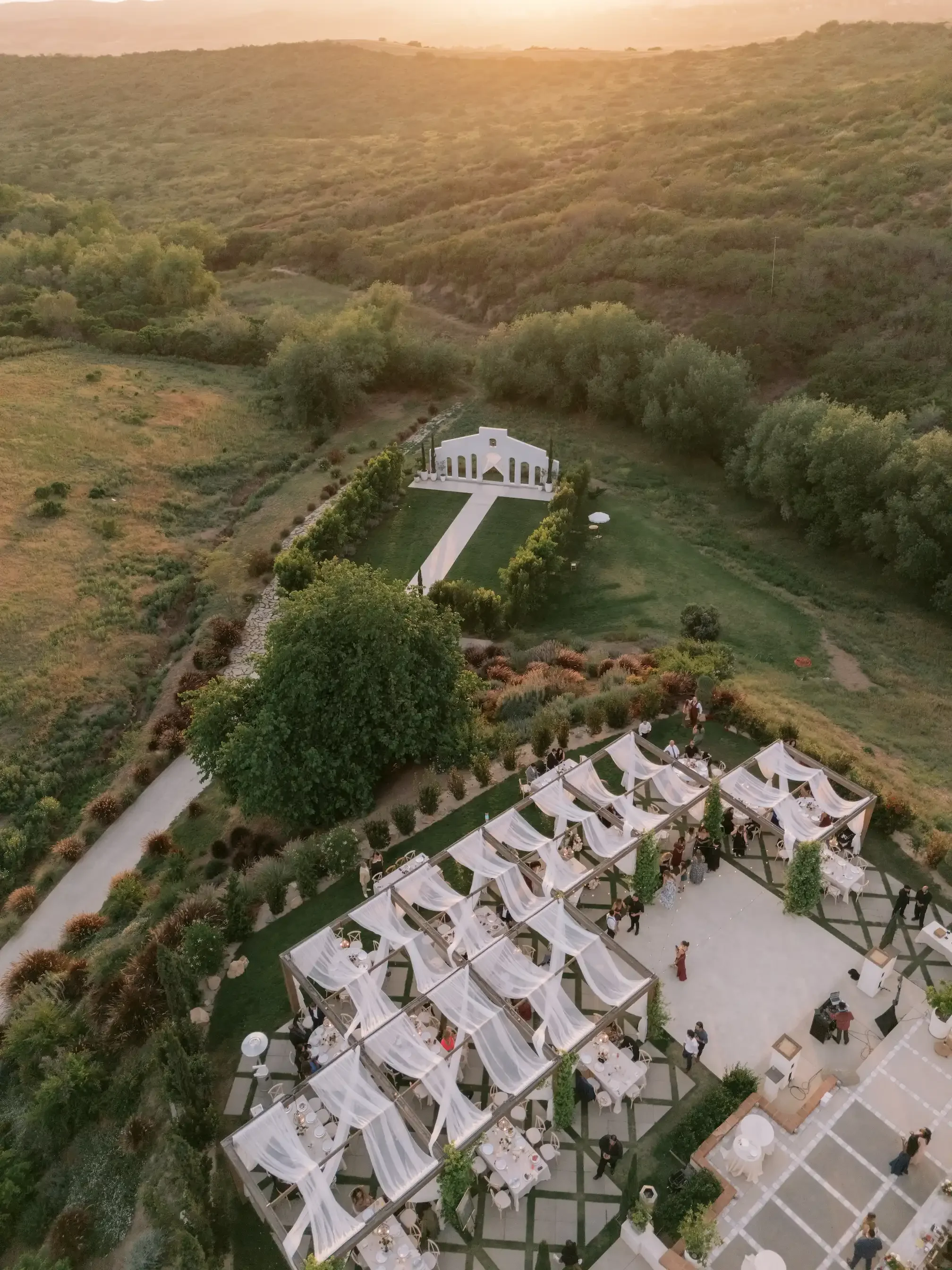 Golden-hour aerial view of the hilltop reception and ceremony chapel at Jeune Perché Estate surrounded by rolling green hills