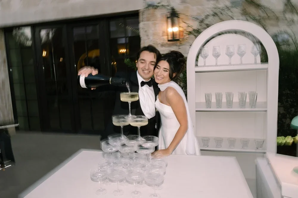 A groom pouring champagne into a champagne tower during his Monserate Winery wedding 