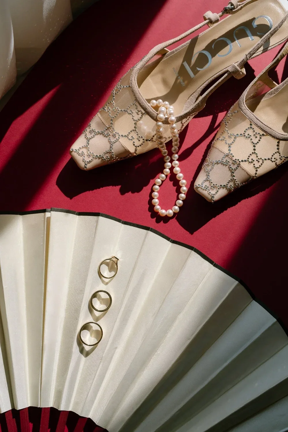 Close-up of wedding details including elegant designer wedding shoes, a pearl necklace, and wedding rings arranged on a fan, captured in Lafayette Hotel in San Diego