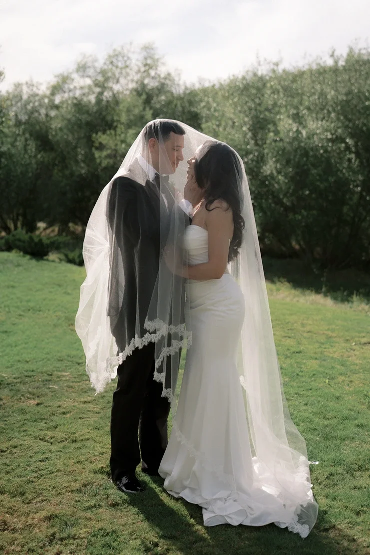 Bride and groom sharing an intimate moment beneath the bride's veil in a grassy field at Jeune Perché Estate