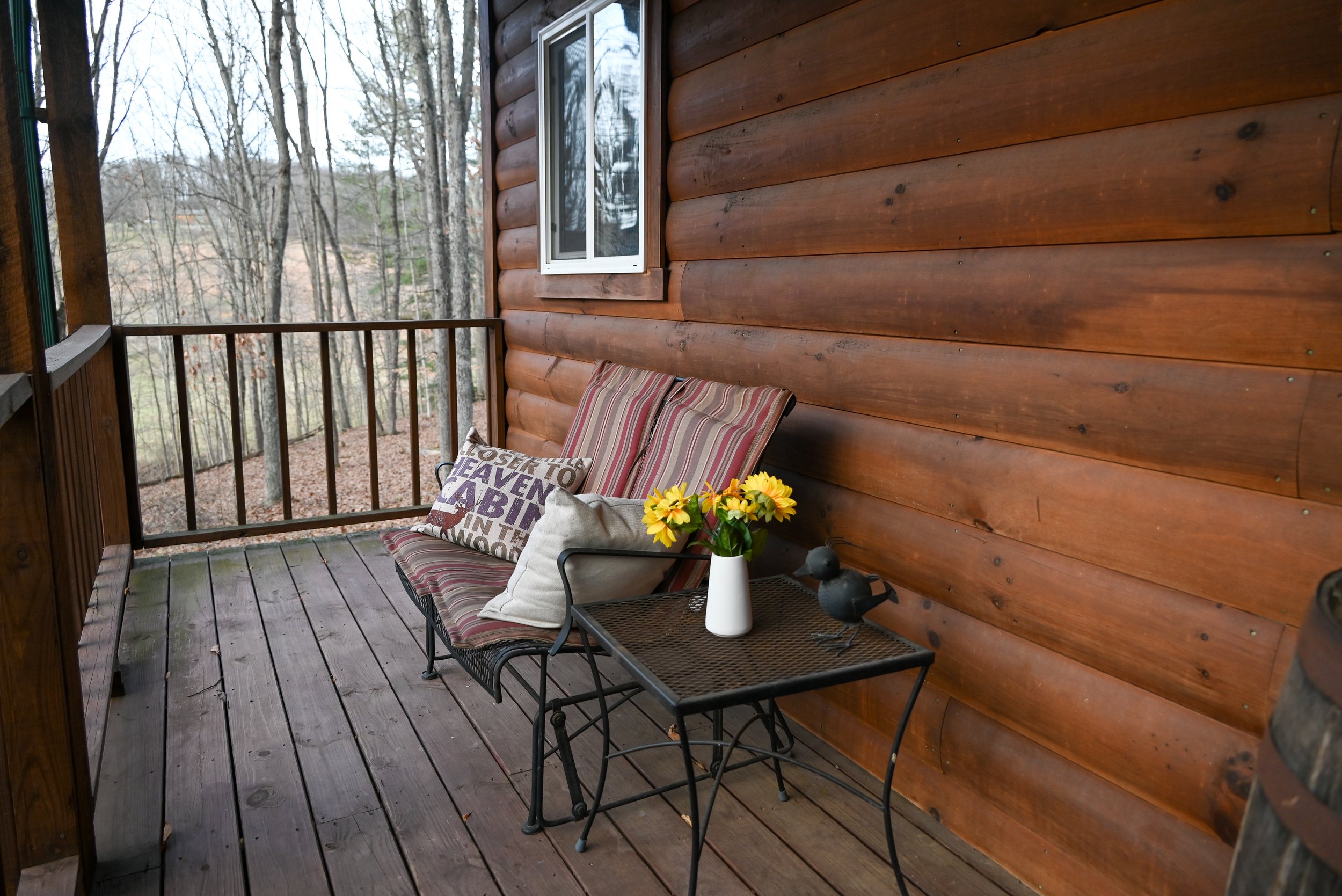 Relaxing porch area at Beary Cozy Cabin with cushioned seating and a table overlooking the wooded Hocking Hills landscape.