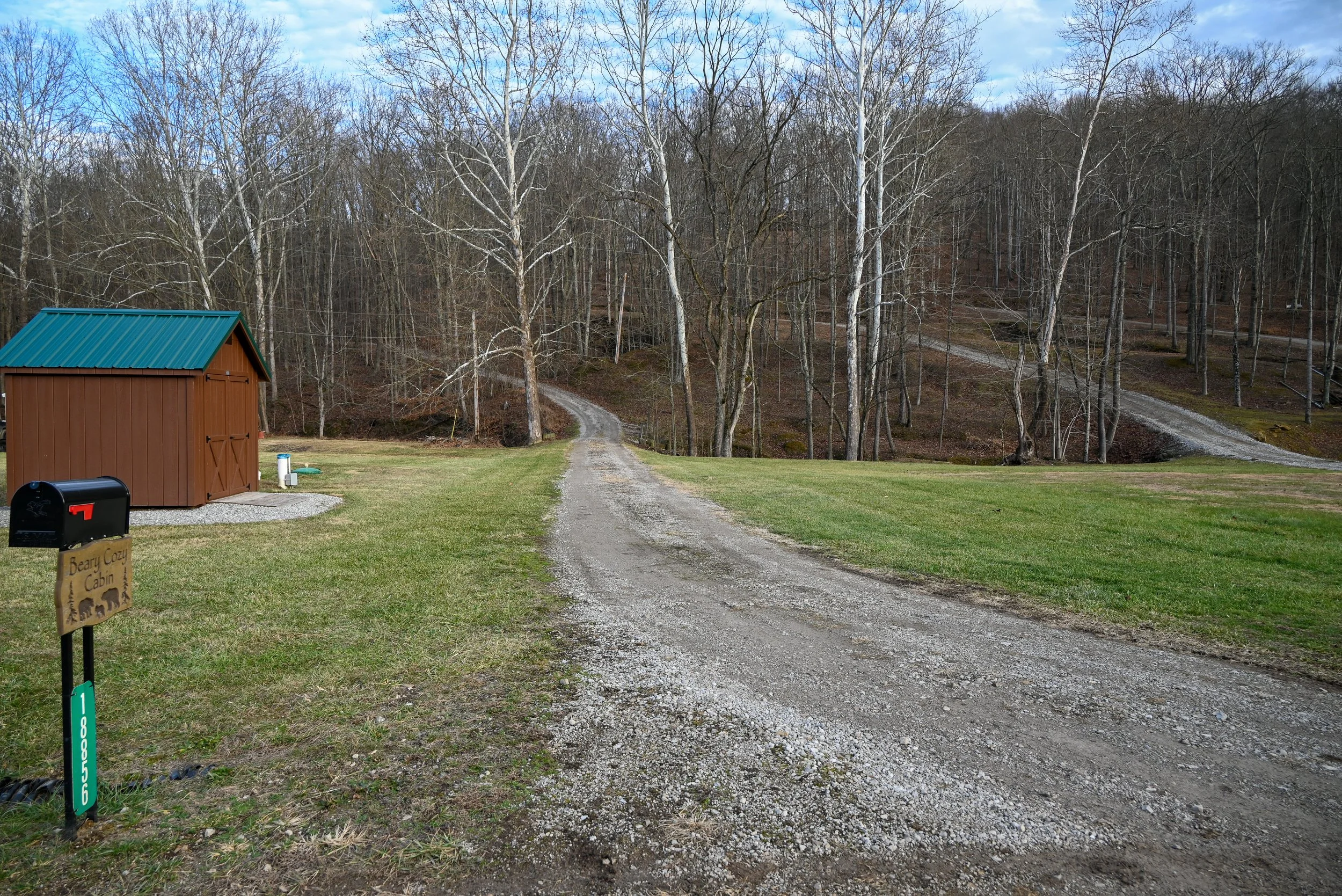 Gravel driveway leading up to Beary Cozy Cabin in Hocking Hills, surrounded by open fields and forested hills.