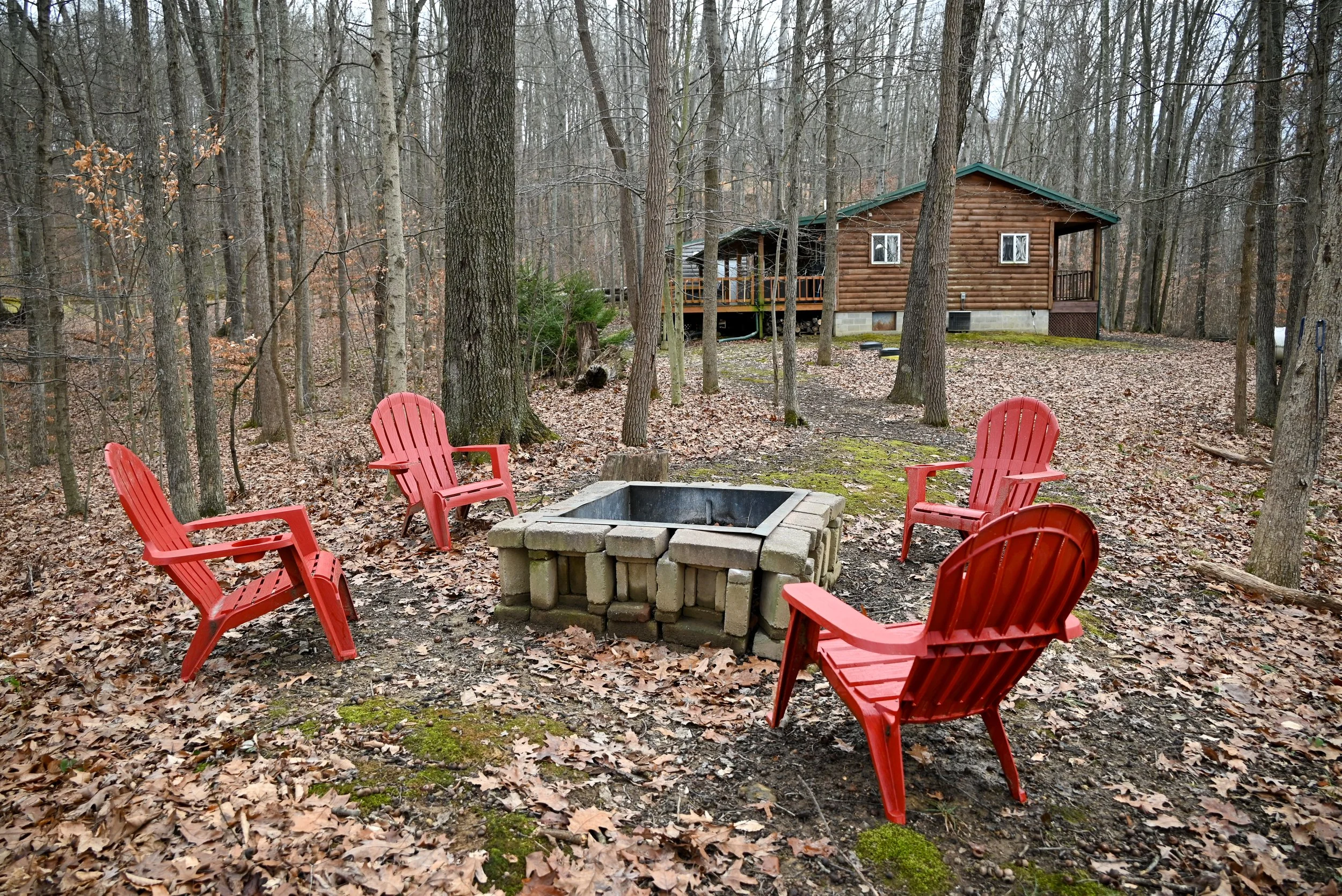 Secluded woodland fire pit with red chairs overlooking the cabin at Beary Cozy Cabin, a romantic, peaceful getaway in Hocking Hills.