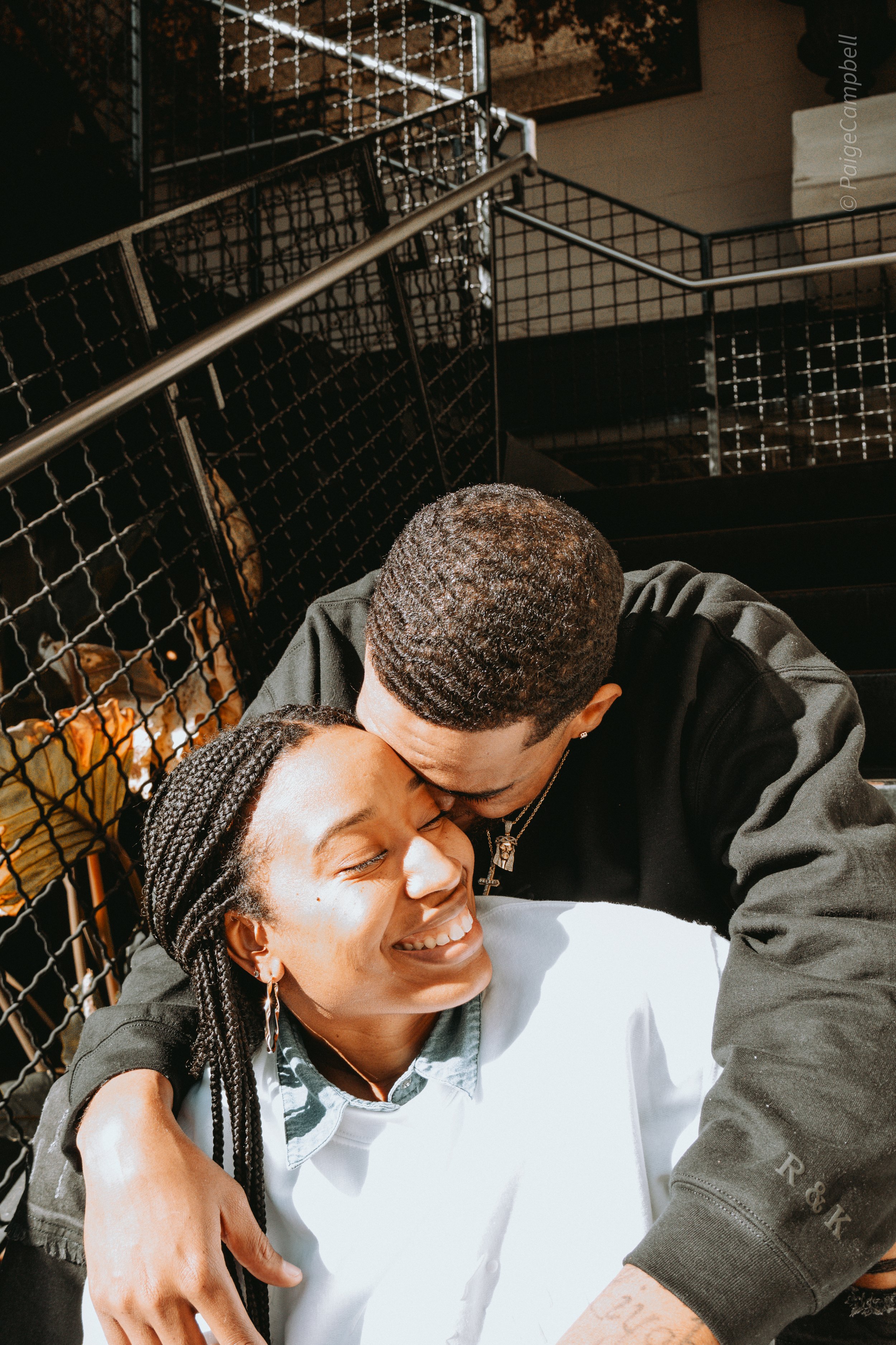 A couple embracing and smiling on a staircase, with metal railing in the background.