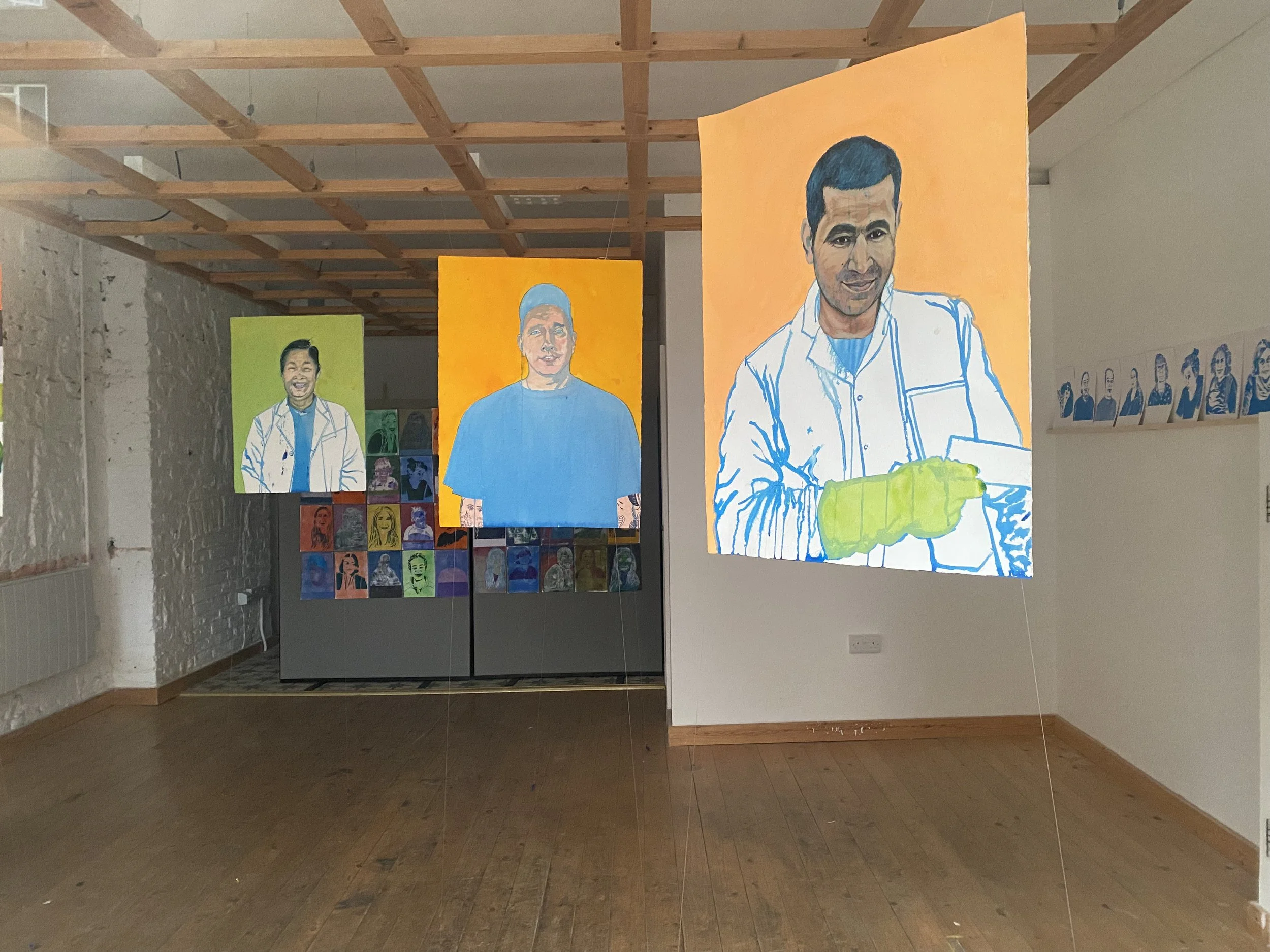 a series of large and colourful portraits of trades people hang, unframed, from the celling