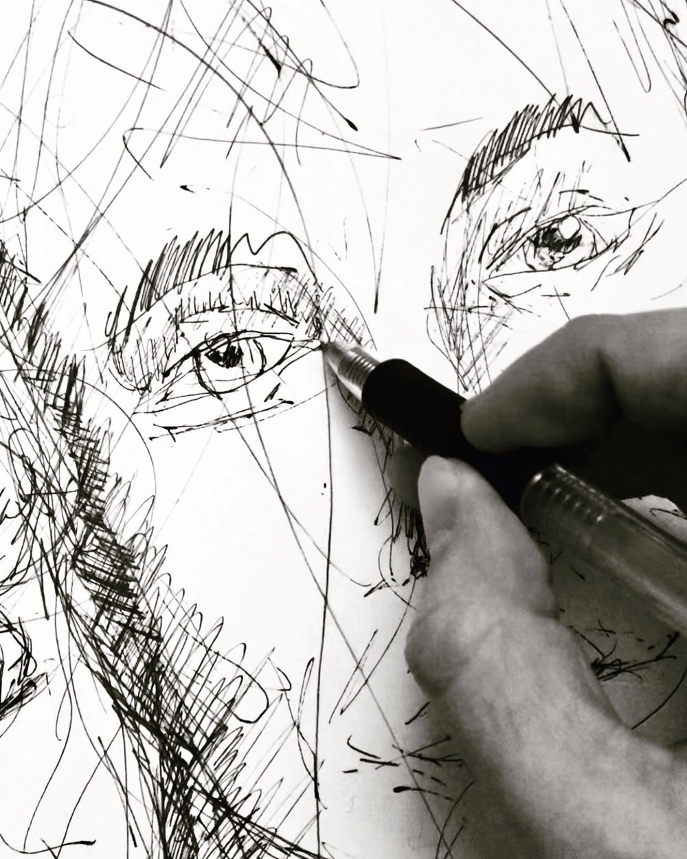 Sketch of two human eyes and eyebrows being drawn on paper with a pen.
