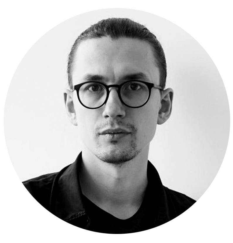 Black and white portrait of Nikolai Karelin, Art Director and concept artist, a man wearing glasses, with his hair tied back, looking directly at the camera.